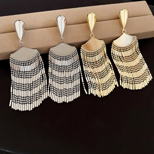 Detailed close-up of gold and silver fan-shaped tassel earrings on a beige display box