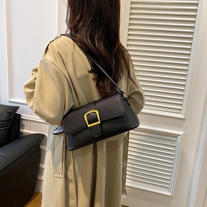 Detail of a chic black leather shoulder bag with a gold buckle worn with a beige trench coat