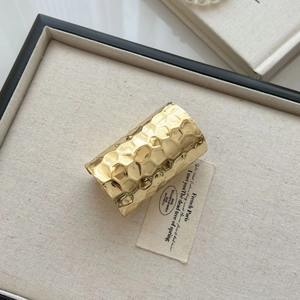 Detail of gold metal cuff bracelet featuring hammered honeycomb texture on display tray