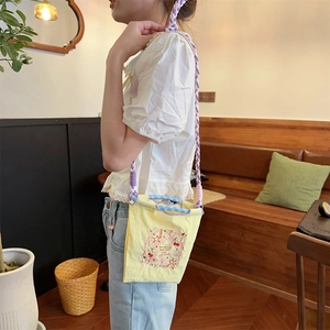 Gros plan du sac en toile jaune brodé avec bandoulière tissée violette sur un mannequin