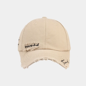Detail of distressed beige cotton baseball cap with vintage embroidery and frayed edges