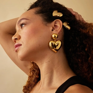 Close-up of polished gold heart-shaped earrings and matching hair accessory on a model