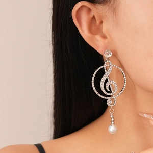 Close-up of silver music note earrings with pavé rhinestones and a white pearl drop