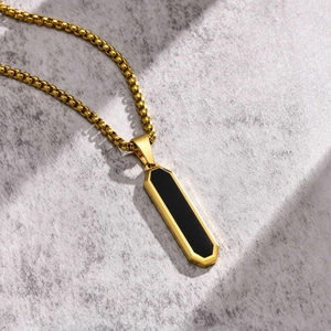 Detail view of a minimalist gold geometric rectangle pendant with black inlay on stone texture