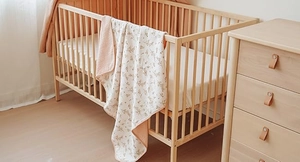 Detail of double-sided cotton baby blanket with floral pattern on a wooden crib