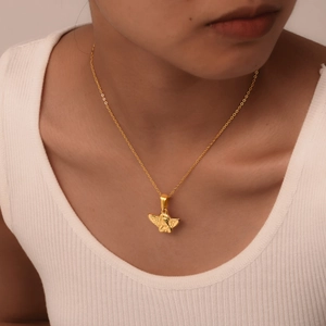 Detail shot of a golden angel pendant necklace worn by a model with warm lighting