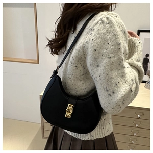Chic black leather hobo bag with gold ring buckle worn as an underarm shoulder bag