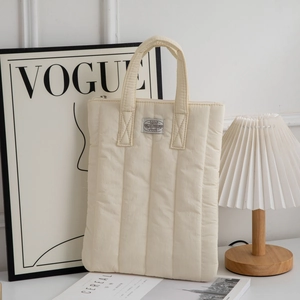 Close-up of cream quilted laptop bag with vertical stitching and woven brand label