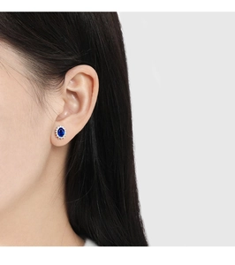 Close-up of royal blue sapphire sunflower stud earrings worn on the ear for scale