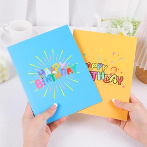 Detail of 3D Happy Birthday pop-up cards in blue and yellow held by hand on a desk