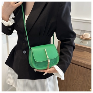 Close-up of vibrant green saddle bag with gold tassel pendant on a stylish model