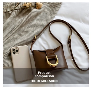 Mini brown leather crossbody bag with gold U-shaped buckle compared to a smartphone