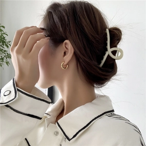 Fashionable gold C-shape hoop earrings and beige hair claw clip worn by a model
