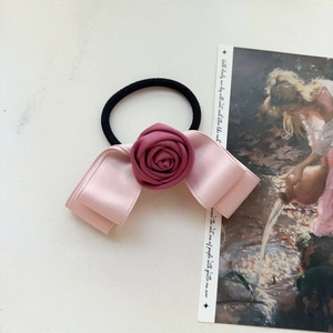 Detail of pink satin bow hair tie with dark pink rose on a black elastic band