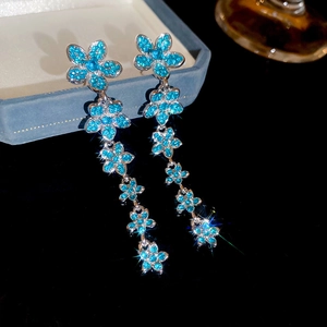 Detail of long blue crystal flower tassel earrings with silver finish on dark mirror