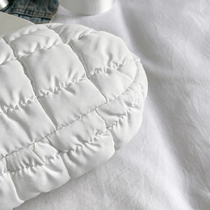 Detail of white quilted fabric texture showing square stitching on a puffer chest bag
