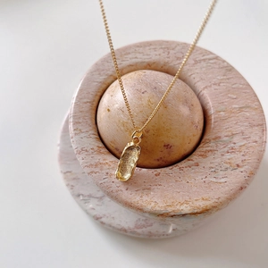 Detail of a 925 sterling silver gold necklace with organic abstract pendant on pink marble