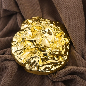 Elegant gold metal accessory with pleated foil texture on a brown textured background