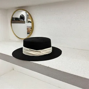 Detalle de sombrero canotier de paja negra con cinta plisada beige y hebilla dorada