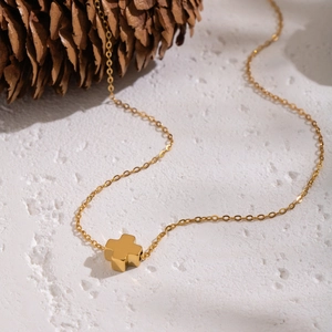 Minimalist gold stainless steel necklace with cross pendant on a white textured surface