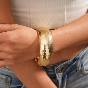 Detailed view of wide gold hammered texture cuff bracelet worn on a minimalist outfit