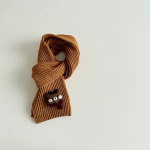 Detail view of caramel knitted scarf with cute teddy bear accent and ribbed texture