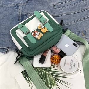 Green and white nylon crossbody bag with cute bear pins and accessories layout