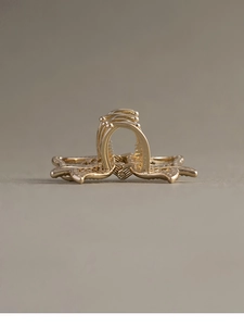 Detailed view of a golden metal bow hair claw clip with pearls on a neutral background
