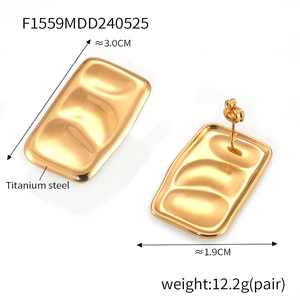 Close-up of golden rectangular earrings with layered concave texture and secure pin closure