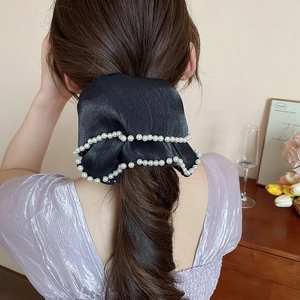 Detail of a large black satin bow hair scrunchie with white pearl trim on long wavy hair