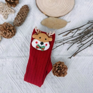 Detail of red Christmas baby socks featuring reindeer patches and knitted cotton texture