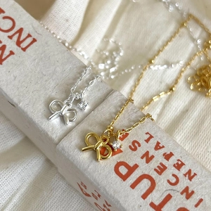 Detail of silver and gold bow necklaces with zircon stones on beige fabric