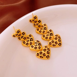Détail macro de boucles d'oreilles cœur léopard en cascade avec strass ambrés sur plateau