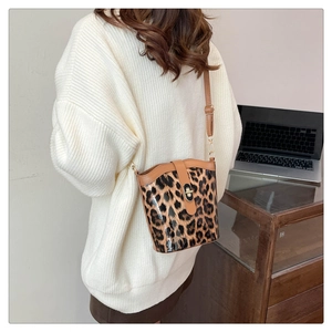 Detail of leopard print bucket bag with metal lock worn over a white sweater