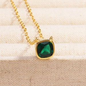 Macro shot of minimalist gold necklace featuring a square emerald-cut green gemstone pendant