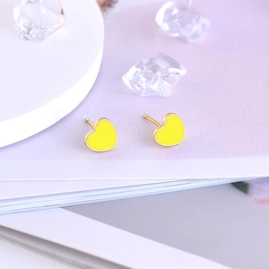 Detail view of yellow enamel heart stud earrings on a light purple background