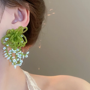 Close-up of handmade floral earrings with green and white seed beads on ear