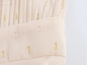 Detail of beige chiffon fabric featuring elegant gold sequins and pleated texture