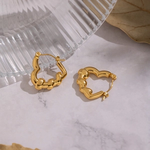 Close-up of golden heart earrings with twisted texture on elegant marble background
