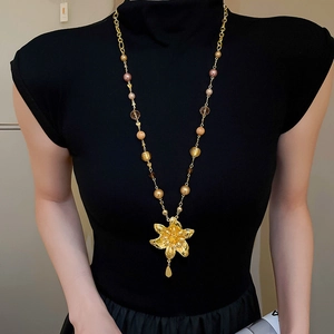 Détail d'un long collier de perles avec pendentif fleur dorée sur une tenue noire sobre