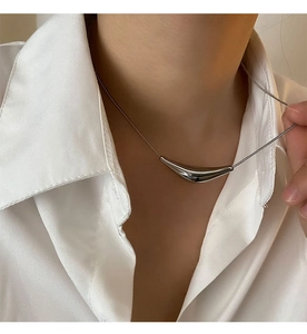 Gros plan d'un pendentif en métal argenté sur une fine chaîne portée par un mannequin