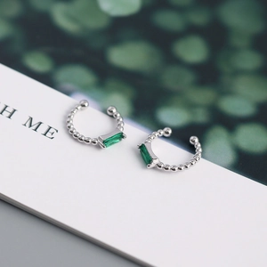 Macro detail of silver ear cuffs featuring emerald-cut green zircon stones on card