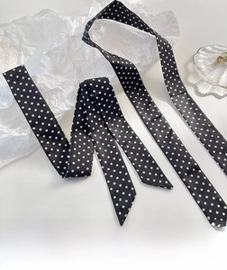 Détail d'un foulard en soie noir à pois blancs sur un plateau en coquillage et papier gaufré