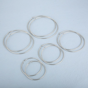 Set of five silver stainless steel hoop earrings in various sizes on a blue surface