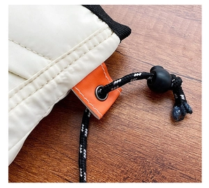 Detail of quilted beige canvas bag featuring orange leather tag and drawstring closure