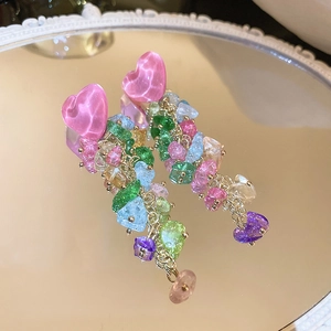 Détail de boucles d'oreilles cœur avec glands en pierres colorées sur un miroir