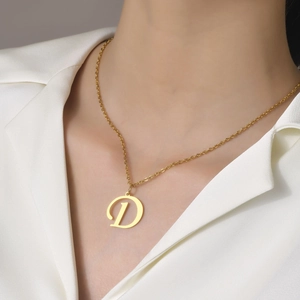 Detail view of a dainty gold chain necklace with a letter D pendant worn by a model