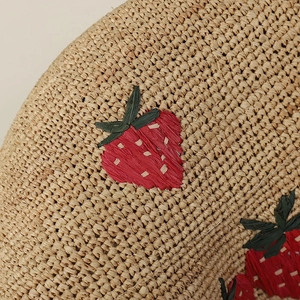Close-up of hand-woven straw hat showing detailed strawberry embroidery and texture