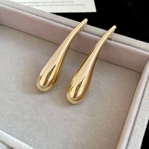 Detailed view of long gold teardrop earrings with a high-polished mirror finish on a tray