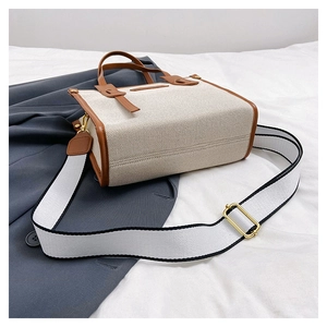 Close-up of contrast canvas tote bag featuring brown leather trim and golden metal hardware